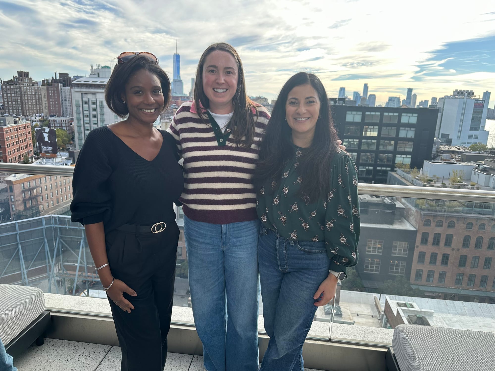 Three Marqii team members smiling on a New York rooftop with the skyline behind them