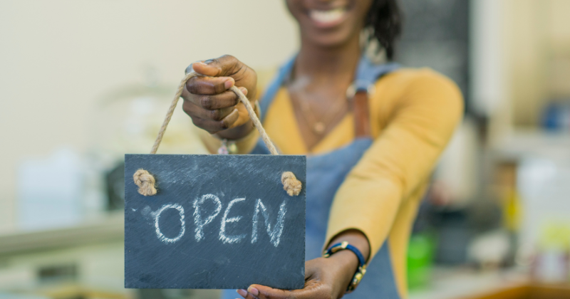 woman in apron holding an open sign
